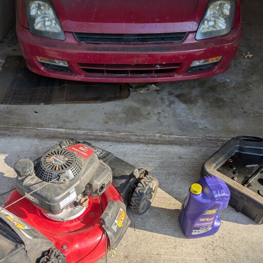A 5 quart jug of Royal Purple engine oil sits next to a Craftsman push mower equipped with a Honda engine and an engine oil catch pan. In the background is a 5th generation Honda Prelude, a sports coupe from the late 90s.